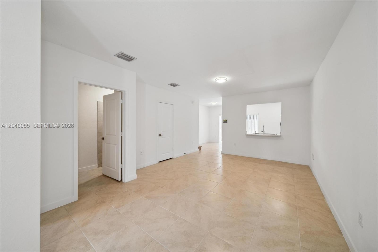 An empty room features white walls, beige tile flooring, and a pass-through kitchen window — 441 NE 4th Ln, Florida City FL 33034, FLORIDA CITY, FL
