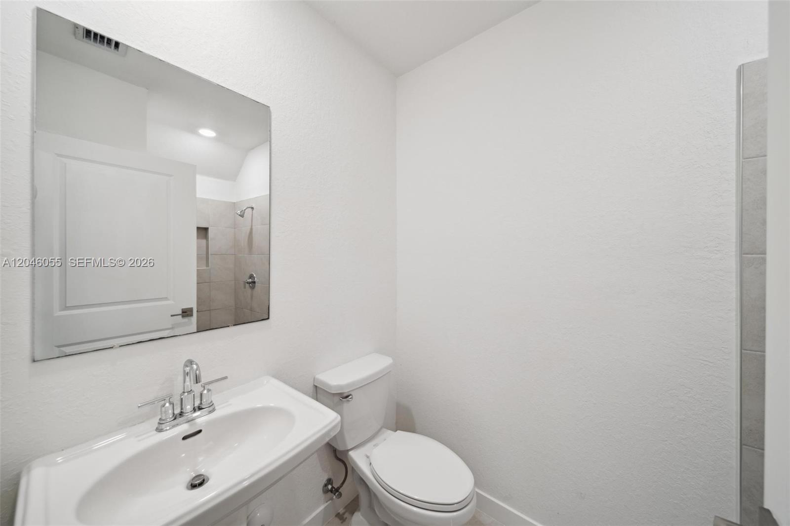 A bathroom features a white pedestal sink, a toilet, and a mirror reflecting a shower — 441 NE 4th Ln, Florida City FL 33034, FLORIDA CITY, FL