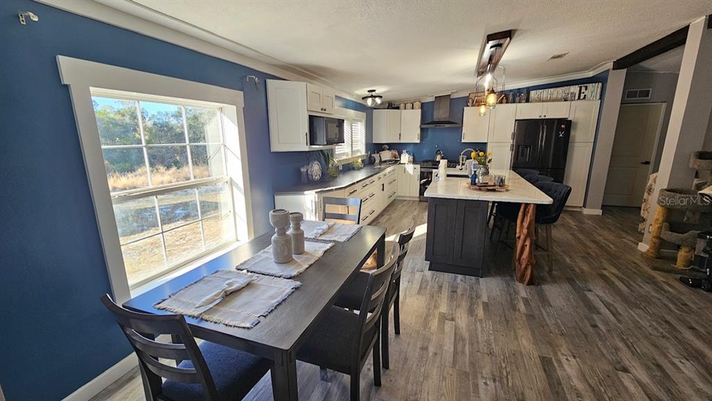 A kitchen and dining area features blue walls, white cabinets, a dark island, and wood-look flooring — 42349 FONSECA LANE, DELAND, FL