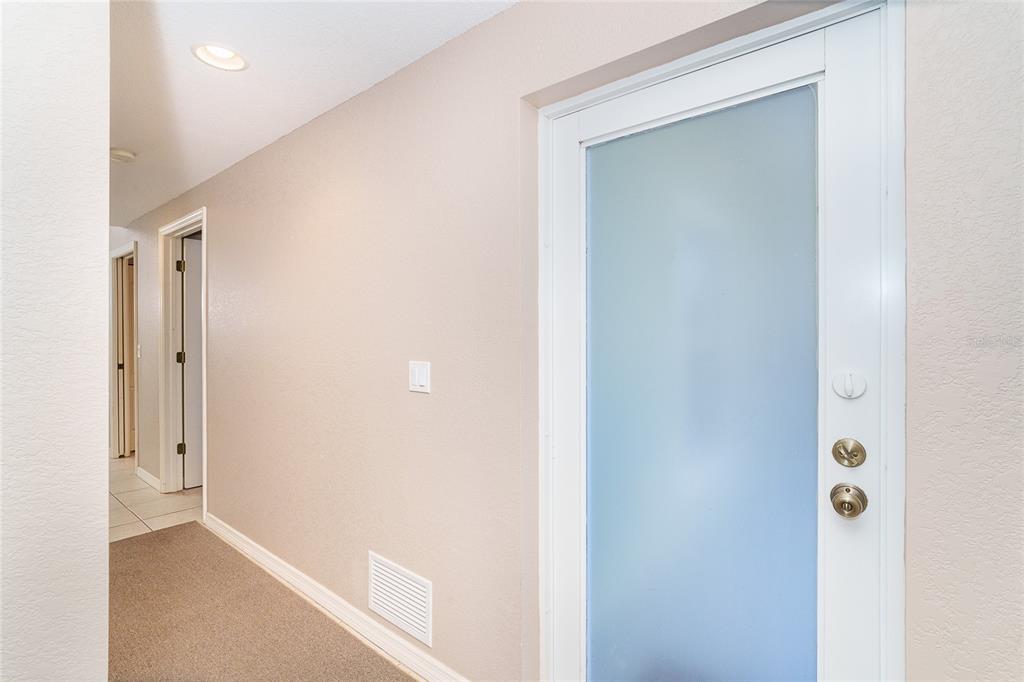 A hallway with beige walls, carpeted flooring, and a white door with a frosted glass panel — 8101 MEMORY LANE UNIT 122, ROTONDA WEST, FL