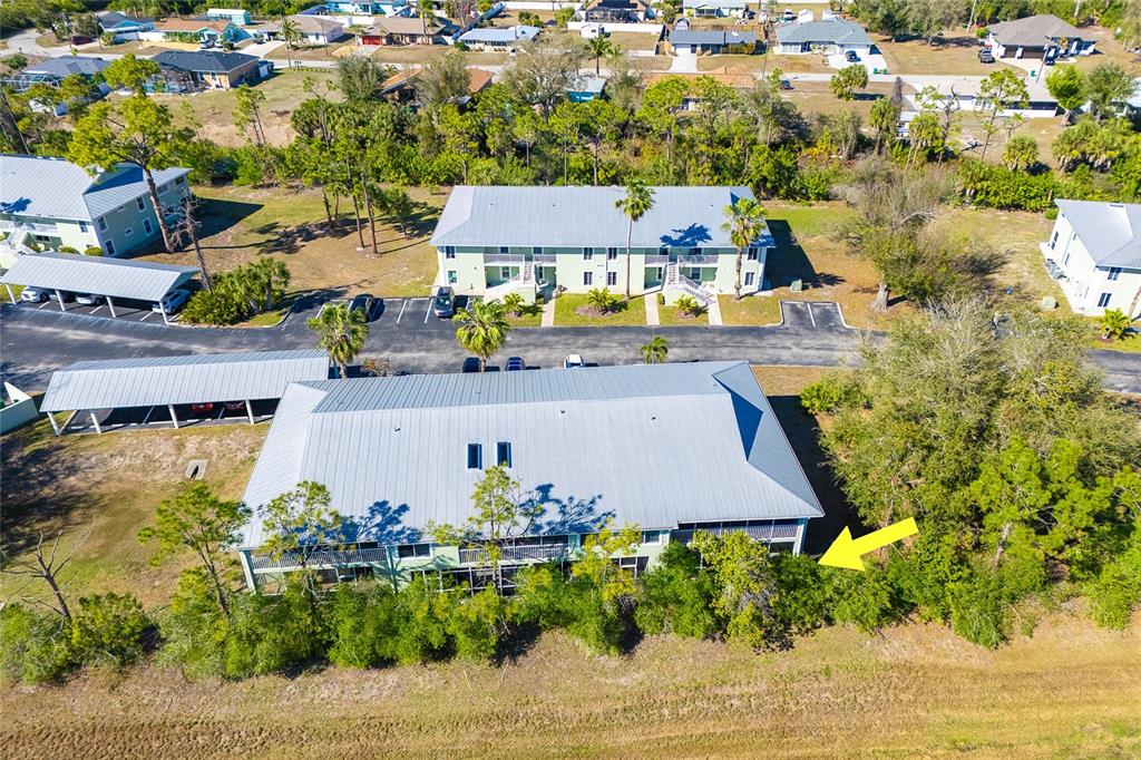 An aerial view shows multi-story apartment buildings with metal roofs and adjacent covered parking — 8101 MEMORY LANE UNIT 122, ROTONDA WEST, FL
