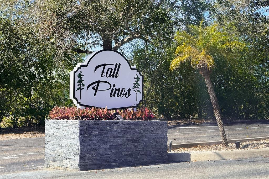 A white sign reading Tall Pines sits atop a stone base near a palm tree — 8101 MEMORY LANE UNIT 122, ROTONDA WEST, FL