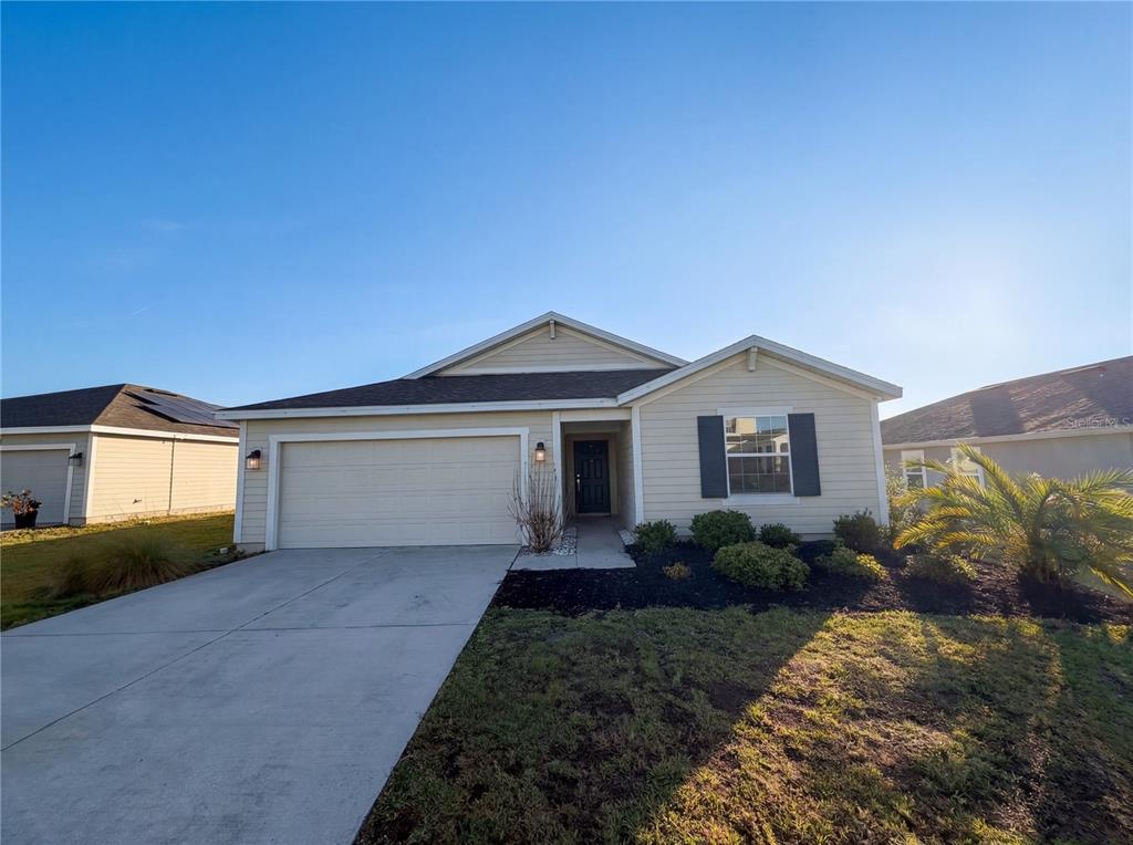 A single-story house with beige siding, a two-car garage, and a front-facing window with shutters — 5108 TANZANITE DRIVE, MOUNT DORA, FL