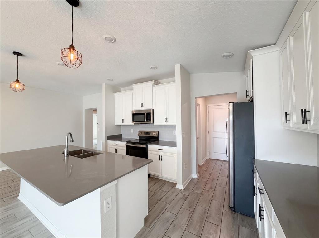 A modern kitchen features white cabinets, a large island with a sink, and tile flooring — 5108 TANZANITE DRIVE, MOUNT DORA, FL