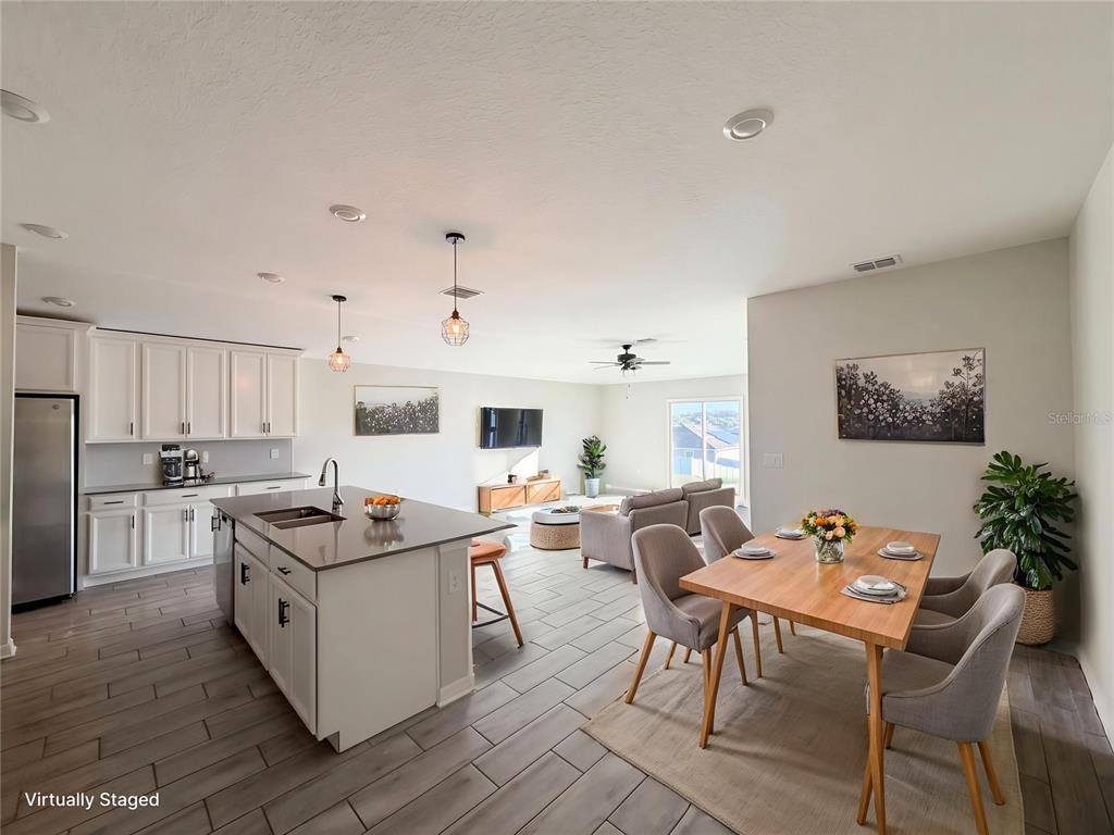 An open-concept kitchen, dining area, and living room featuring white cabinets and tile flooring — 5108 TANZANITE DRIVE, MOUNT DORA, FL