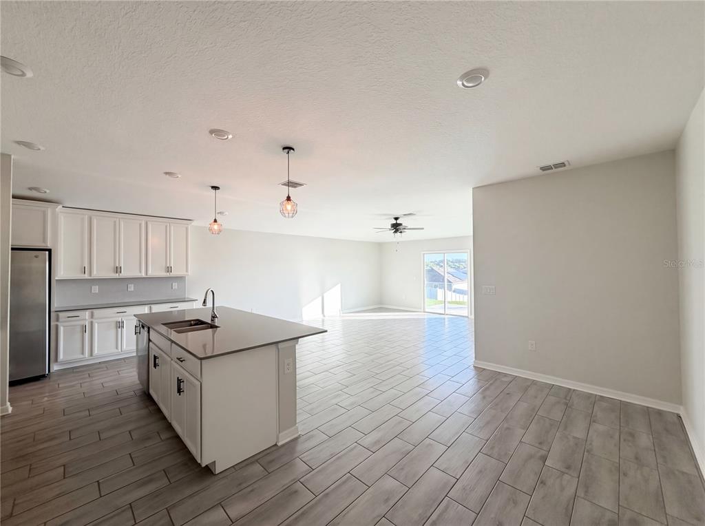 A kitchen with white cabinets, a central island, and gray tile flooring opens to a living area — 5108 TANZANITE DRIVE, MOUNT DORA, FL