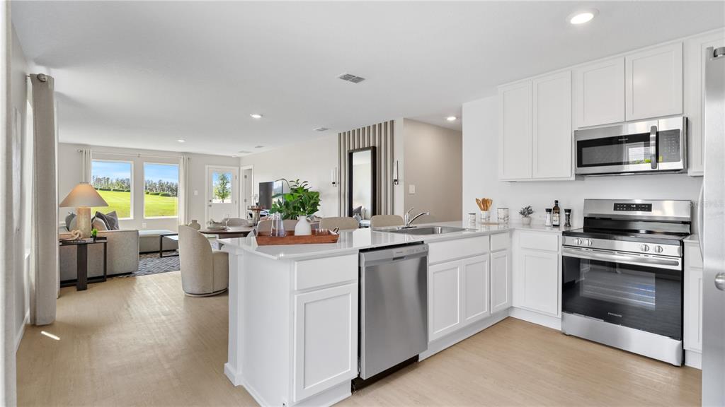 A modern kitchen with white cabinets and stainless steel appliances overlooks an open living area — 611 CHANNEL WAY, GROVELAND, FL