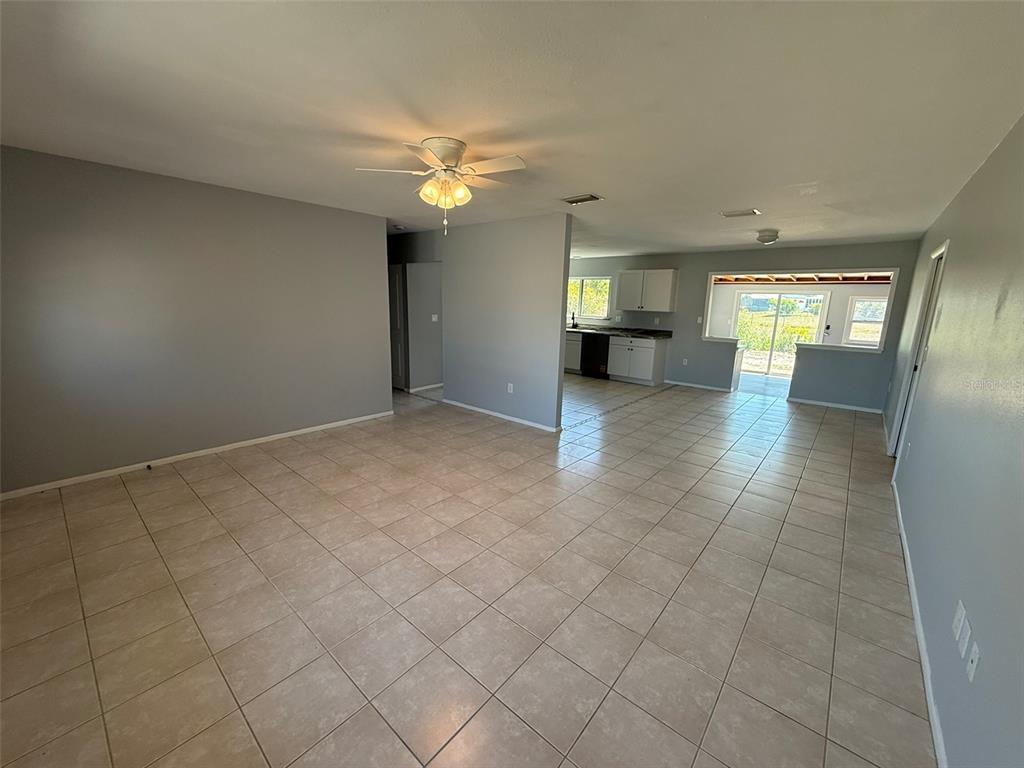 An open-concept living area with light gray walls and beige tile flooring leads to a kitchen — 3236 MONTCLAIR CIRCLE, NORTH PORT, FL