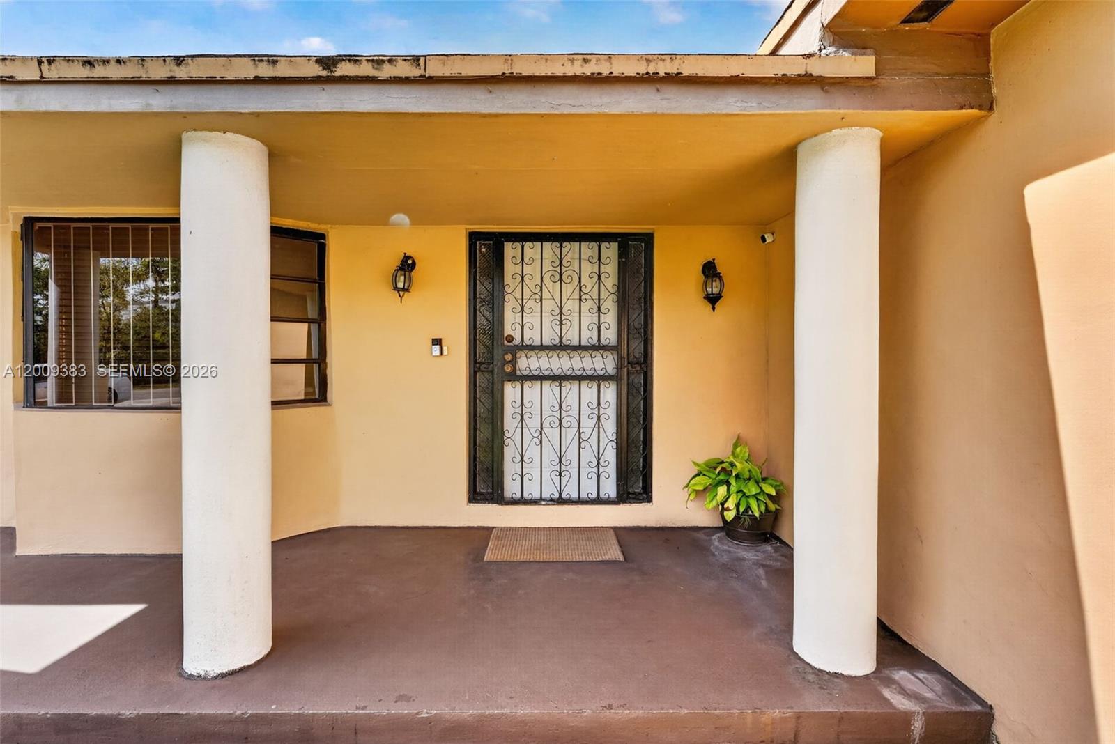 A covered porch features two white columns, a decorative security door, and a potted plant — 2450 NW 108th St, Miami FL 33167, MIAMI, FL
