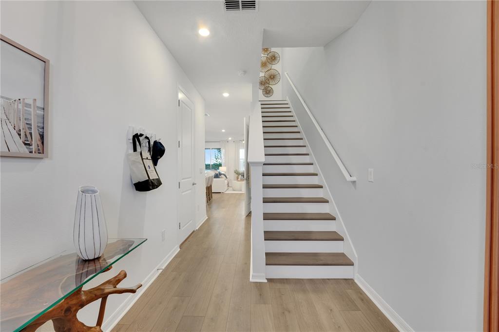 A bright entryway features light wood flooring, a staircase with white railings, and a console table — 31825 KESTREL CALLING DRIVE, SAN ANTONIO, FL