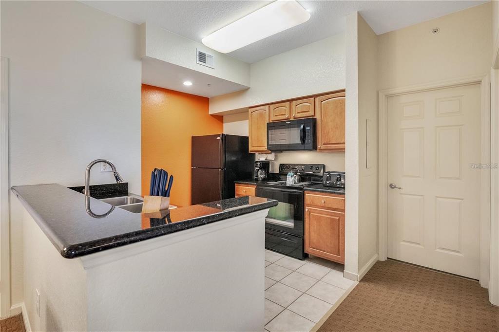 A kitchen features dark countertops, wooden cabinets, black appliances, and an orange accent wall — 8101 RESORT VILLAGE DRIVE UNIT 3905, ORLANDO, FL