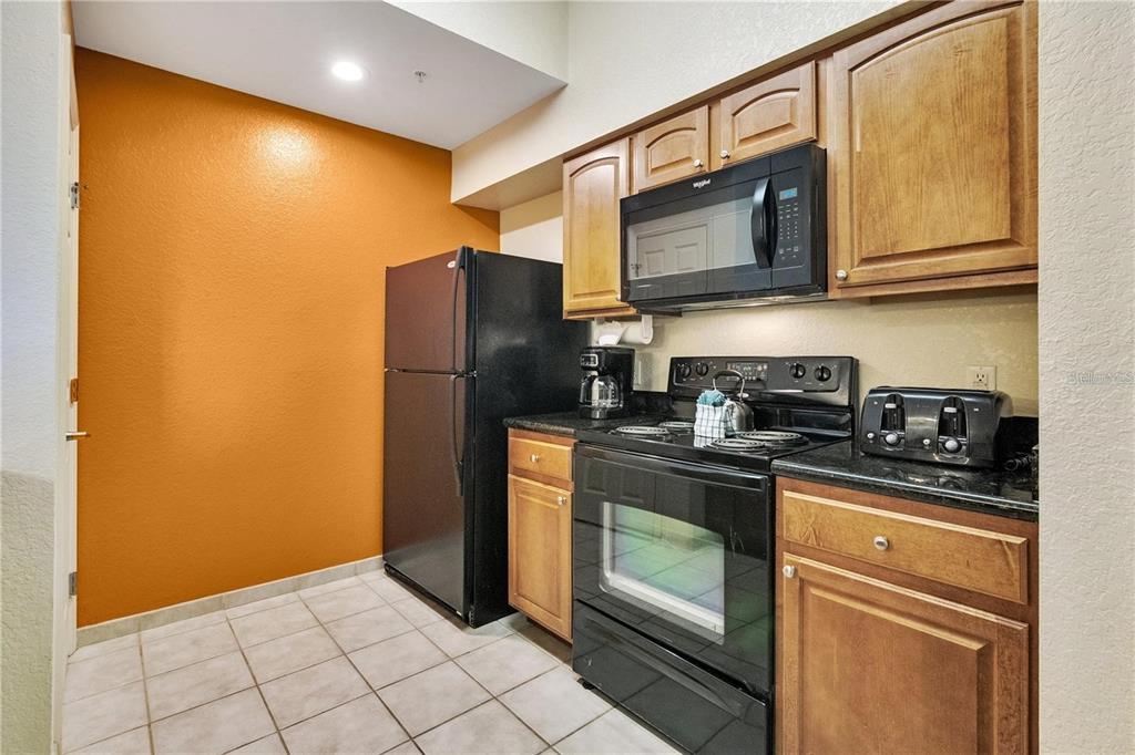 A kitchen features wood cabinets, black appliances, dark countertops, and an orange accent wall — 8101 RESORT VILLAGE DRIVE UNIT 3905, ORLANDO, FL