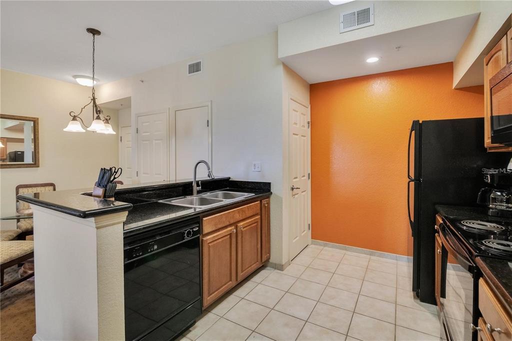 A kitchen features black appliances, wood cabinets, black countertops, and an orange accent wall — 8101 RESORT VILLAGE DRIVE UNIT 3905, ORLANDO, FL