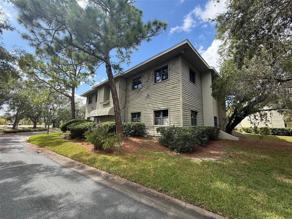 A two-story building with light-colored horizontal siding is surrounded by trees and landscaping — 2841 EXECUTIVE DRIVE UNIT 200, CLEARWATER, FL