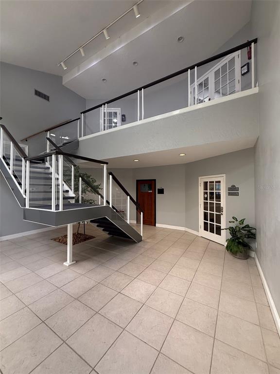 A modern lobby features a floating staircase, tiled floors, and a second-floor balcony railing — 2841 EXECUTIVE DRIVE UNIT 200, CLEARWATER, FL