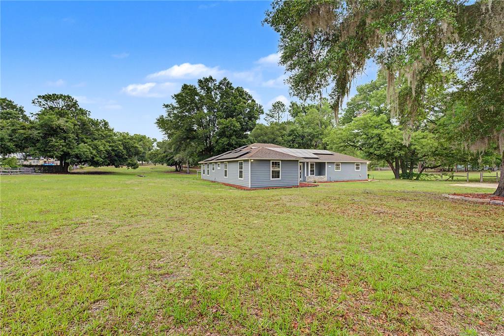 A single-story gray house with a solar panel roof sits on a large grassy lot — 5160 NE COUNTY ROAD 340, HIGH SPRINGS, FL