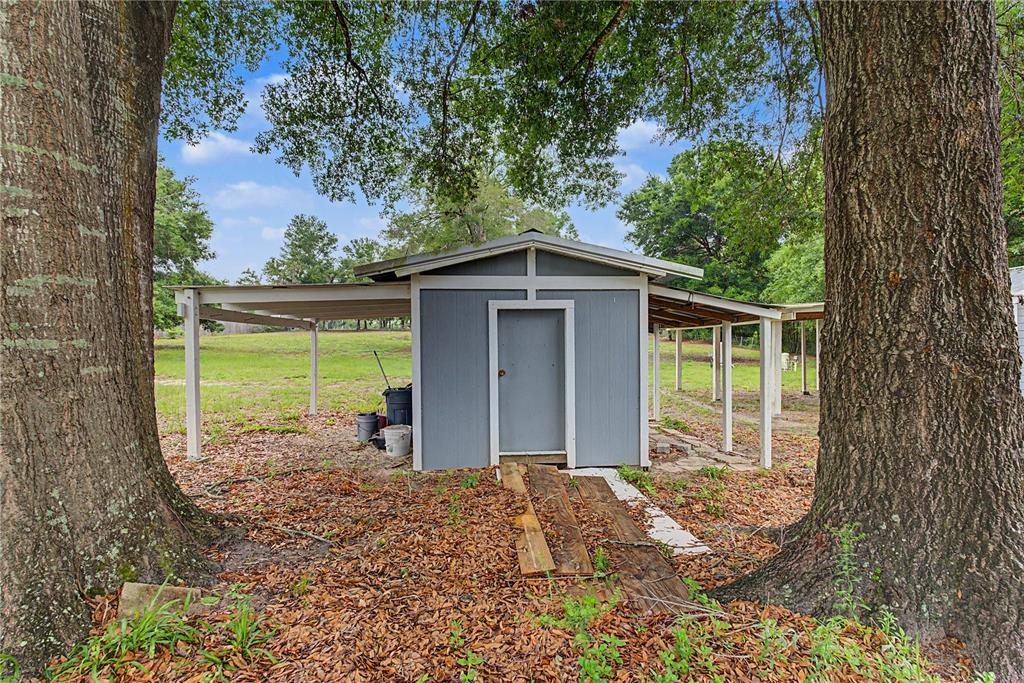A small gray shed with an attached carport stands between two large trees — 5160 NE COUNTY ROAD 340, HIGH SPRINGS, FL