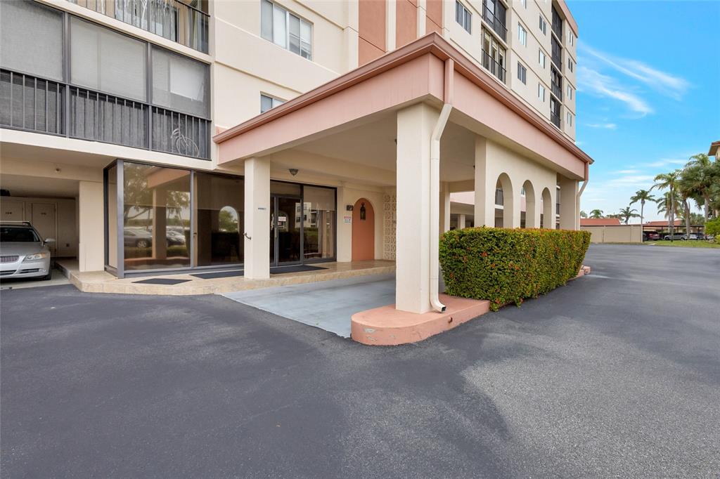 A covered entrance area with a beige overhang and a hedge leads to a building — 19029 US HIGHWAY 19 N UNIT 9-308, CLEARWATER, FL