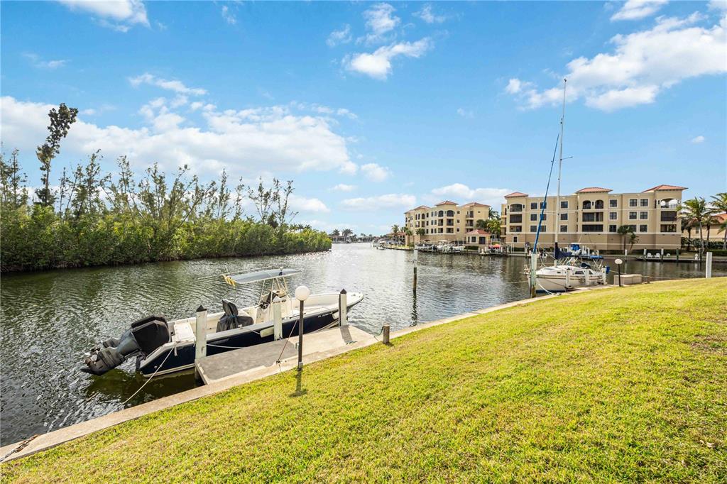 A boat is docked at a grassy waterfront area near a multi-story apartment building — 3256 WHITE IBIS COURT UNIT 324, PUNTA GORDA, FL