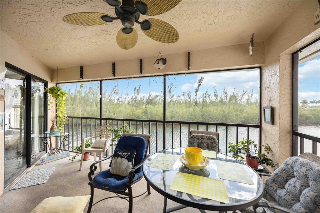 A screened-in porch features a glass dining table, wicker chairs, and a ceiling fan — 3256 WHITE IBIS COURT UNIT 324, PUNTA GORDA, FL
