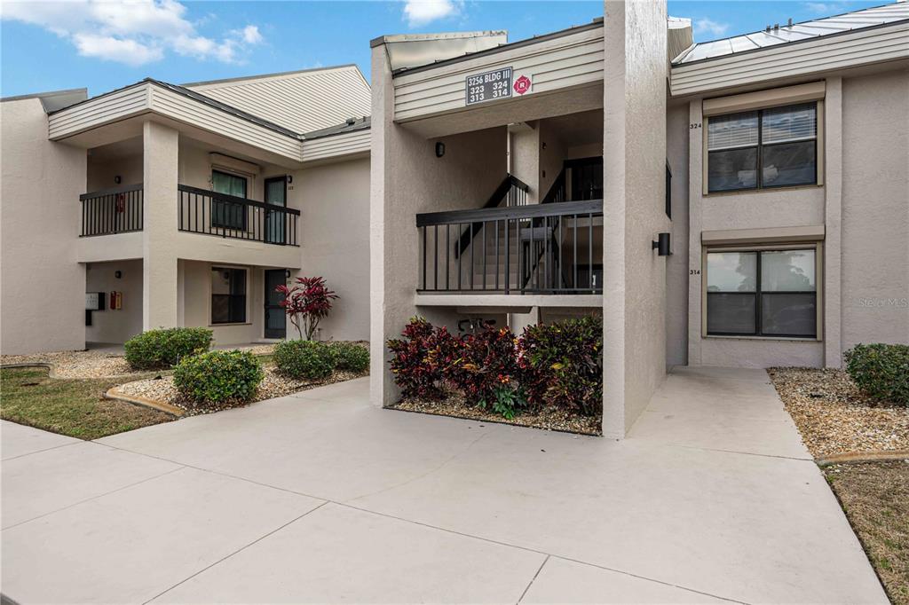 A two-story apartment building exterior features tan stucco walls, black railings, and landscaped bushes — 3256 WHITE IBIS COURT UNIT 324, PUNTA GORDA, FL