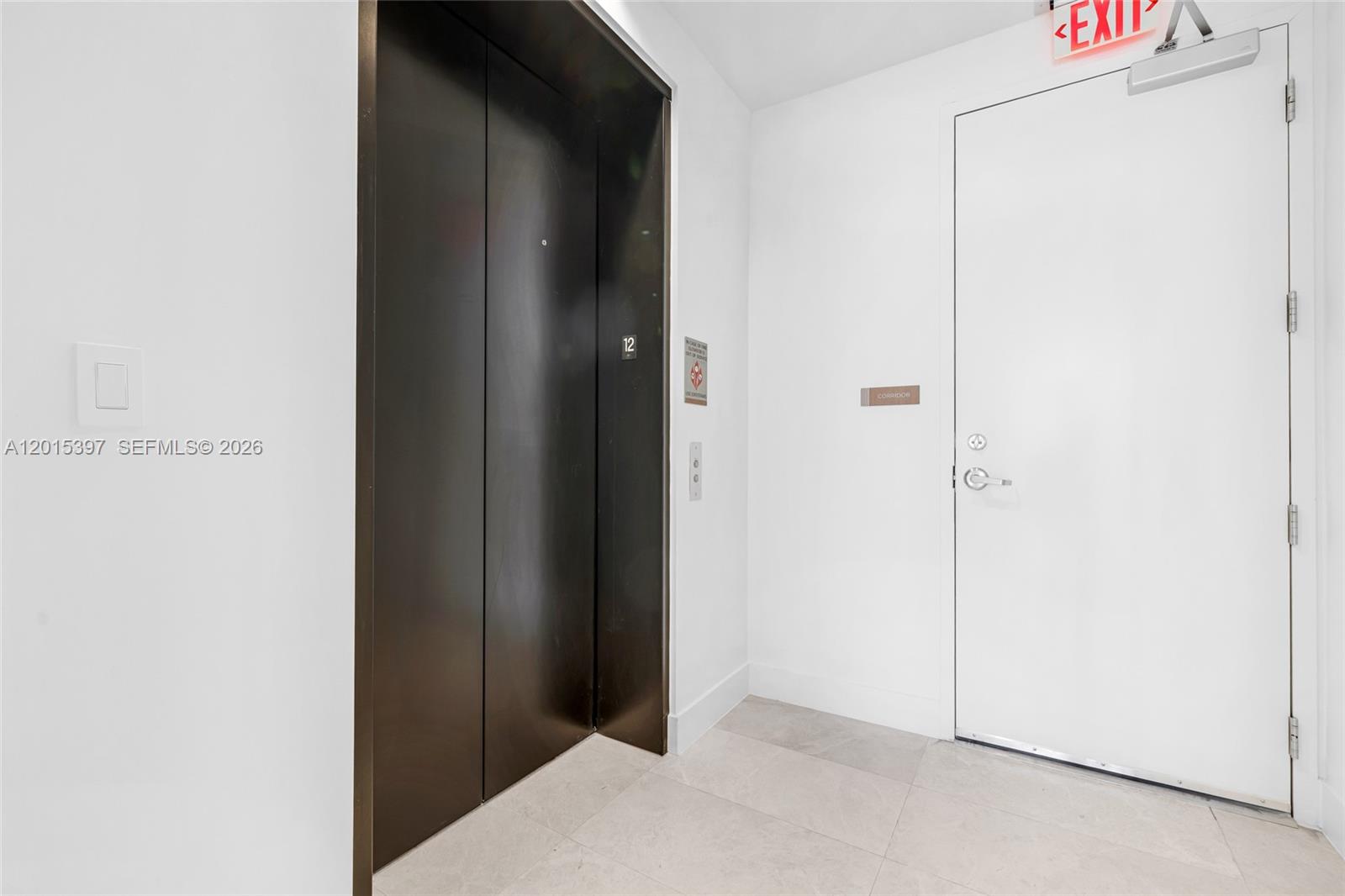 An elevator with dark doors sits next to a white exit door in a hallway — 175 SE 25 Road # 1203, Miami FL 33129, MIAMI, FL