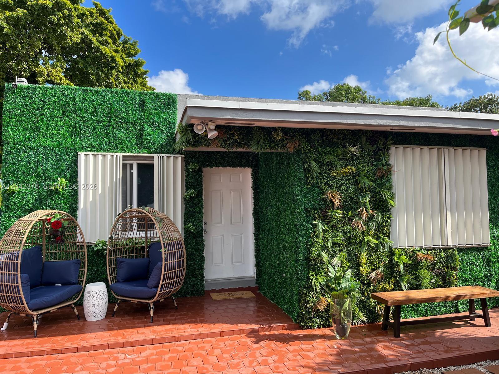 The exterior of a house features a green artificial plant wall, a white door, and patio furniture — 2737 NW 13th Ave, Miami FL 33142, MIAMI, FL