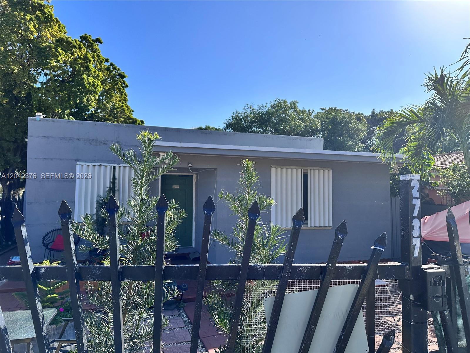 A gray single-story house is viewed from behind a black metal fence — 2737 NW 13th Ave, Miami FL 33142, MIAMI, FL