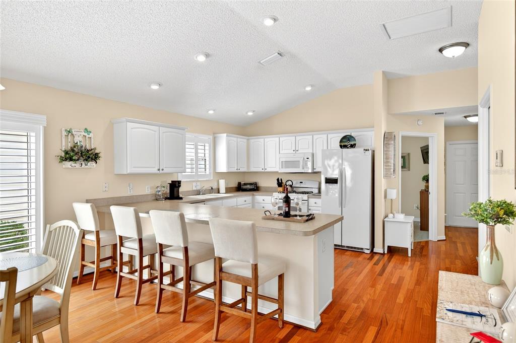 A kitchen features white cabinetry, a breakfast bar with four chairs, and hardwood flooring — 600 AUDREY LANE, THE VILLAGES, FL