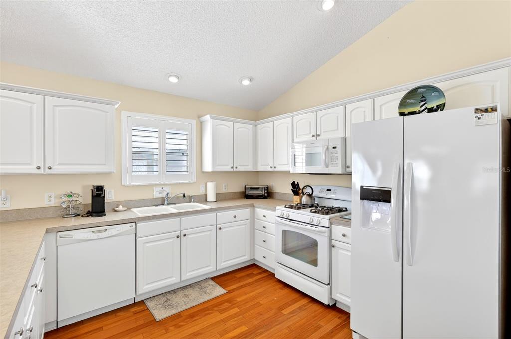 A kitchen features white cabinetry, white appliances, a double sink, and hardwood flooring — 600 AUDREY LANE, THE VILLAGES, FL