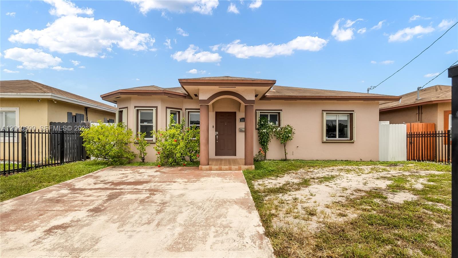 A single-story stucco house features a brown front door, a concrete driveway, and landscaping — 18815 NW 37th Ave, Miami Gardens FL 33056, MIAMI GARDENS, FL