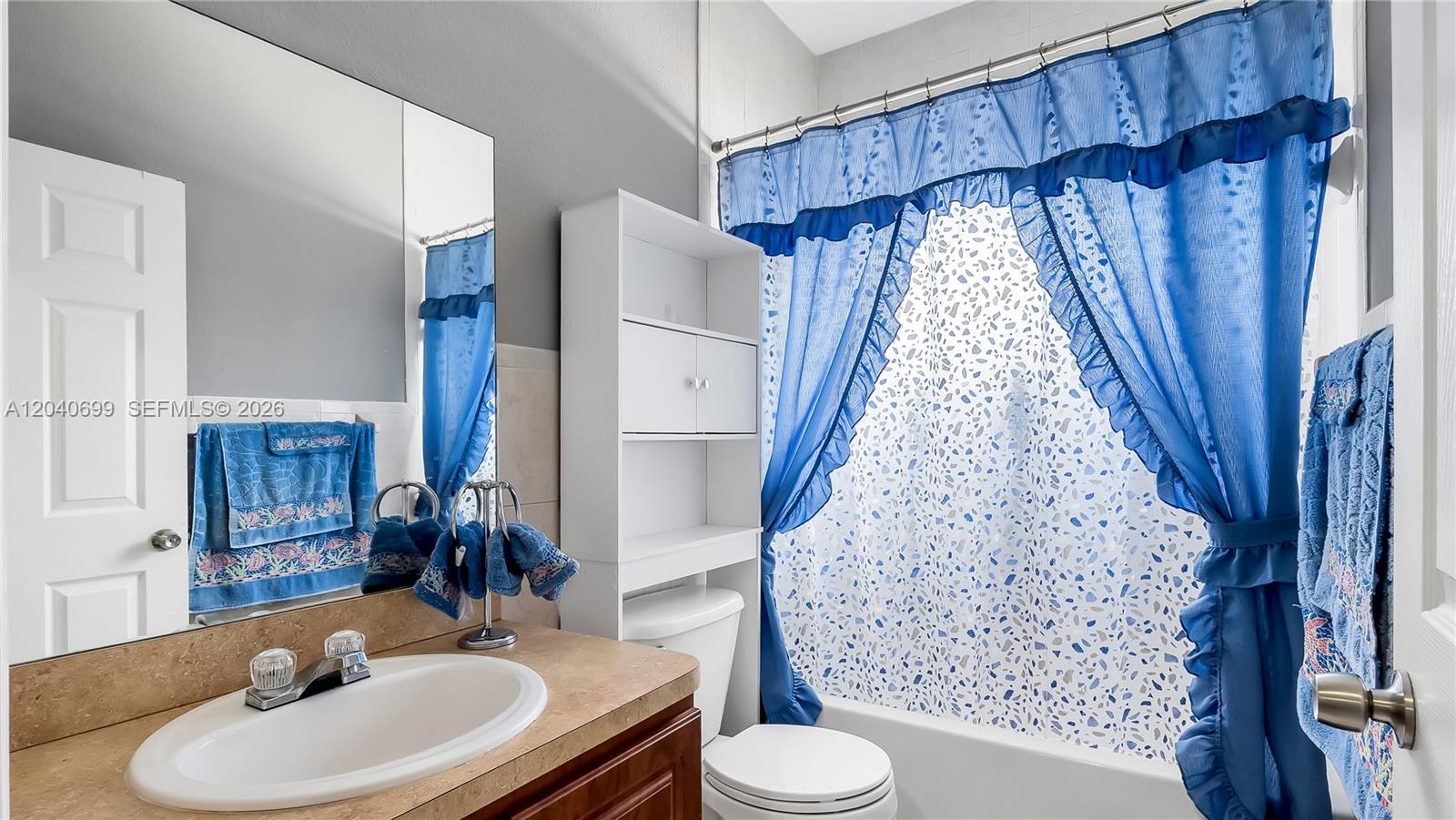 A bathroom features a vanity with a tan countertop, a toilet, and a blue shower curtain — 18815 NW 37th Ave, Miami Gardens FL 33056, MIAMI GARDENS, FL