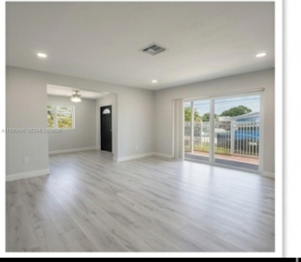 A bright living room features light wood-look flooring, recessed lighting, and large sliding glass doors — 2373 NW 33rd St, Miami FL 33142, MIAMI, FL