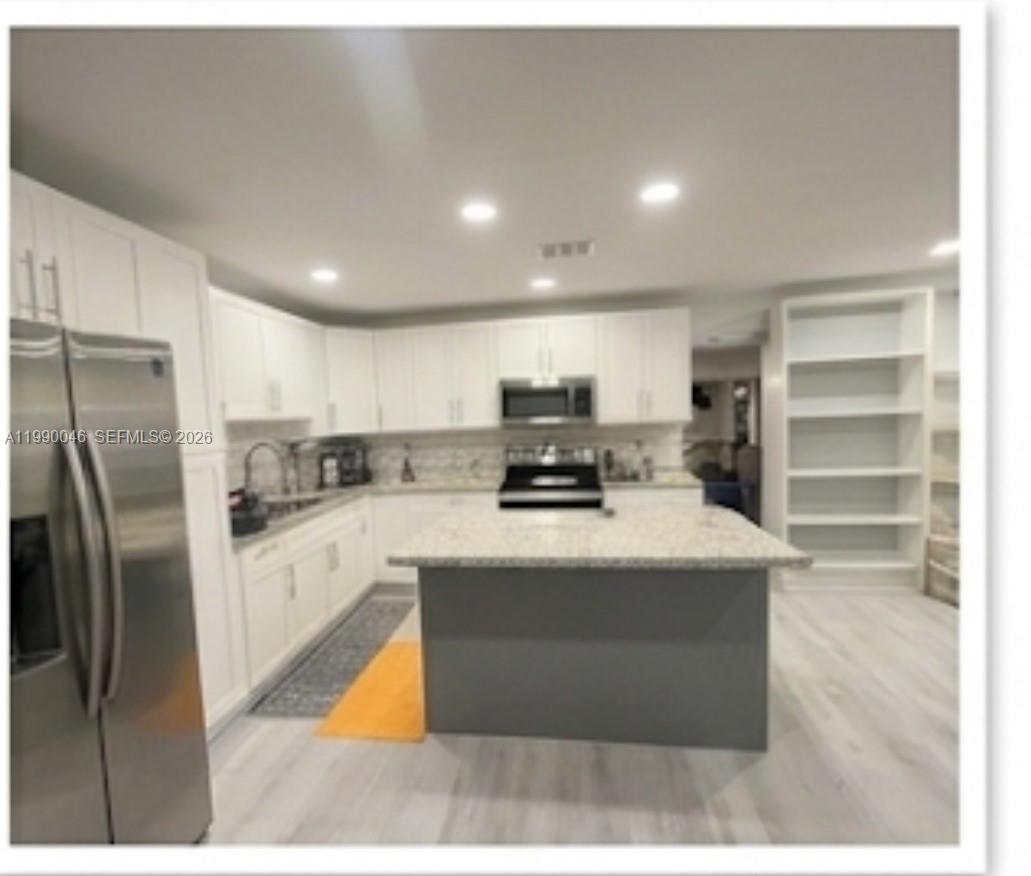 A modern kitchen features white cabinetry, a gray island, stainless steel appliances, and light flooring — 2373 NW 33rd St, Miami FL 33142, MIAMI, FL