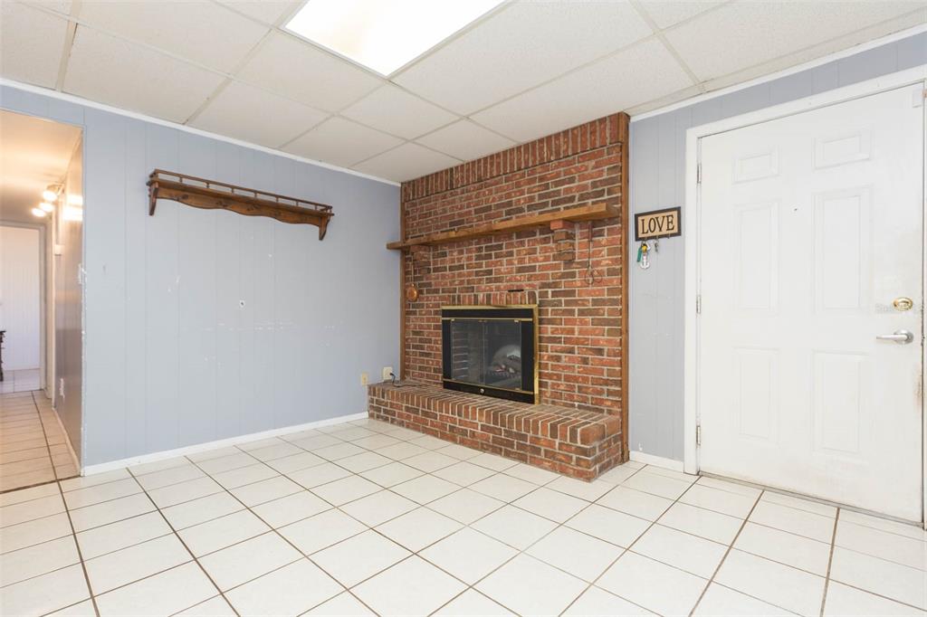 A room with light blue walls, a brick fireplace, white tile flooring, and a drop ceiling — 4102 W FAIRVIEW HEIGHTS, TAMPA, FL
