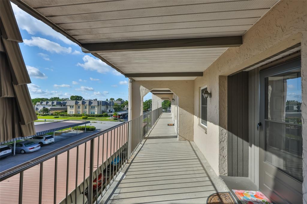 An outdoor covered walkway with a metal railing overlooks a parking lot and apartment buildings — 8703 BARDMOOR BOULEVARD UNIT 303, SEMINOLE, FL