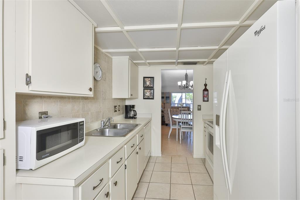 A galley-style kitchen features white cabinets, a white microwave, and a tiled backsplash — 8703 BARDMOOR BOULEVARD UNIT 303, SEMINOLE, FL