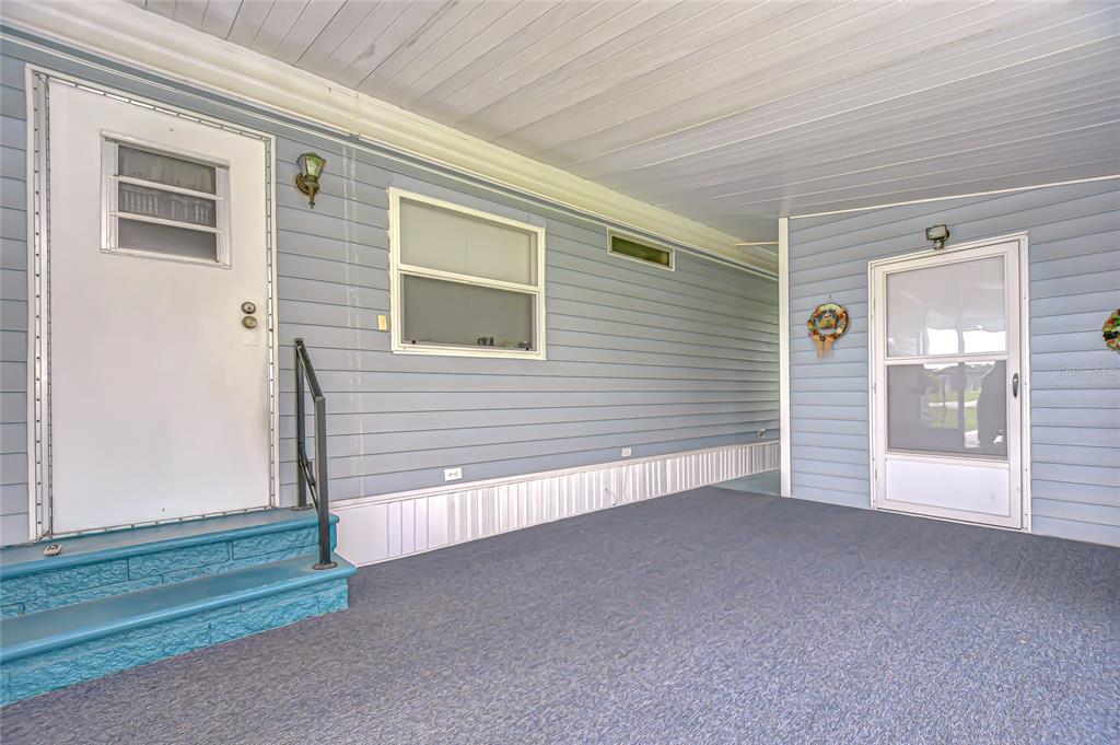A covered outdoor patio with blue siding, two doors, and a set of blue steps — 39443 ELGIN DRIVE, ZEPHYRHILLS, FL