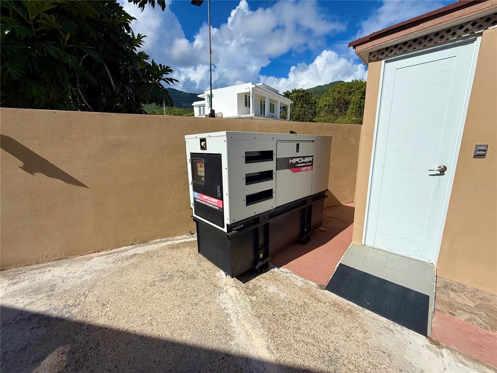 A white Hipower backup generator sits on a concrete patio next to a storage shed — carr #3 JUST 1 MINUTE BEACH, PATILLAS, PR