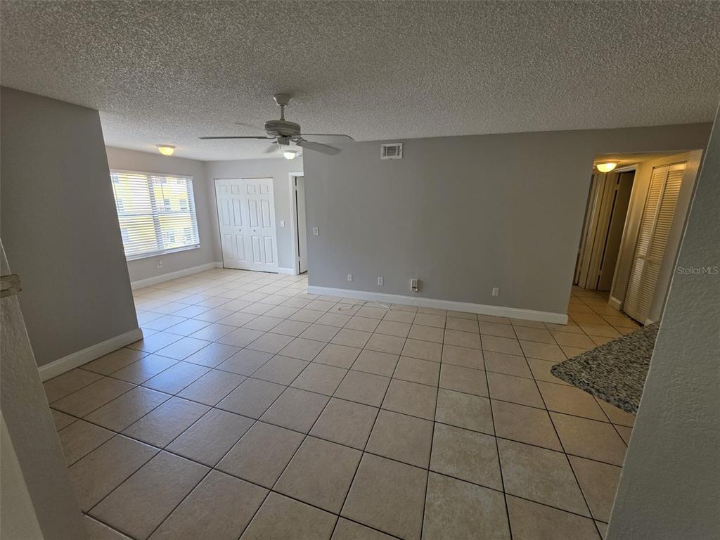 An empty living room features beige tile flooring, gray walls, and a ceiling fan — 4532 COMMANDER DRIVE UNIT 2127, ORLANDO, FL