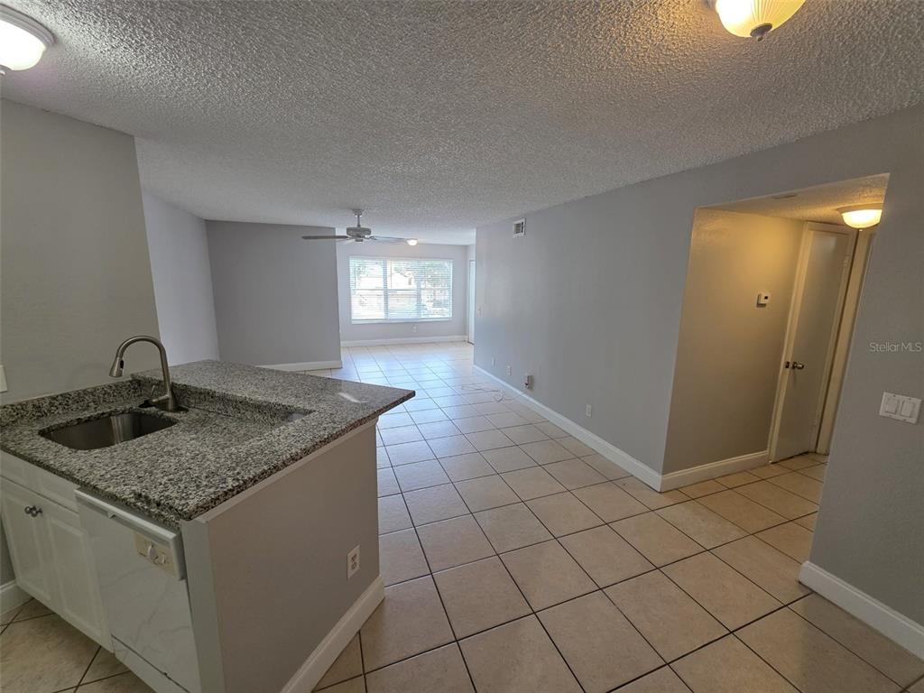 A kitchen with granite countertops overlooks an open-concept living area with tile flooring — 4532 COMMANDER DRIVE UNIT 2127, ORLANDO, FL
