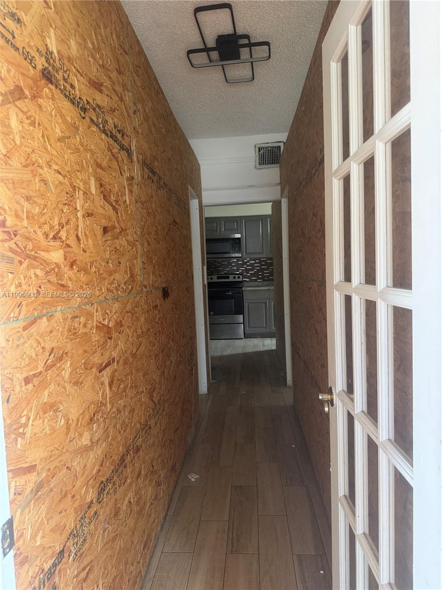 A narrow hallway with unfinished OSB wood walls leads to a kitchen with gray cabinets — 634 SW 10th Ave, Miami FL 33130, MIAMI, FL