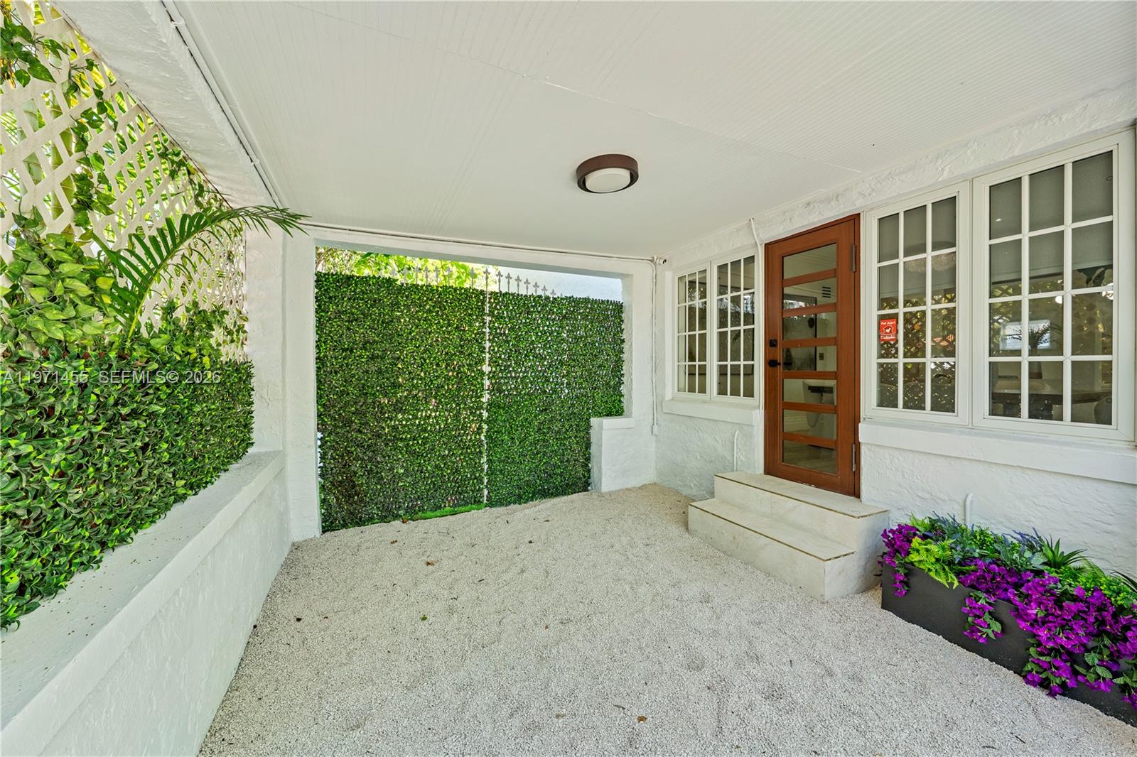 A covered patio features white walls, a gravel floor, a wooden door, and artificial greenery — 178 NE 45th St, Miami FL 33137, MIAMI, FL