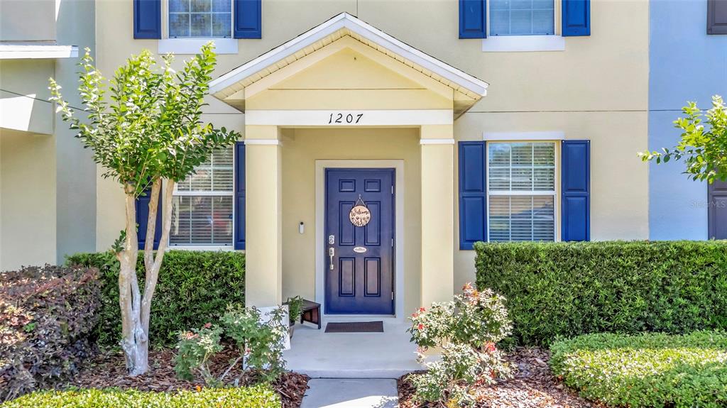 A two-story townhouse exterior with a blue front door, shutters, and a concrete walkway — 1207 ALSTON BAY BOULEVARD, APOPKA, FL