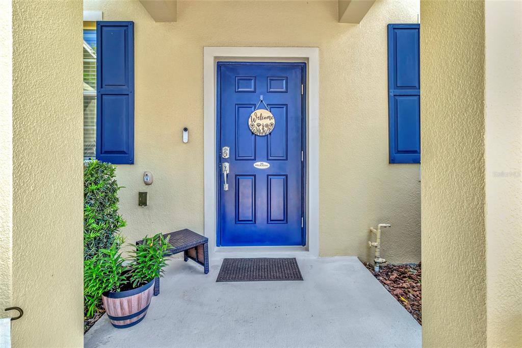 A blue front door with a welcome sign sits on a concrete porch with shutters — 1207 ALSTON BAY BOULEVARD, APOPKA, FL