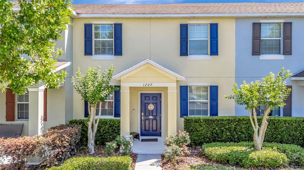 A two-story townhouse exterior features yellow and blue siding with a dark blue front door — 1207 ALSTON BAY BOULEVARD, APOPKA, FL