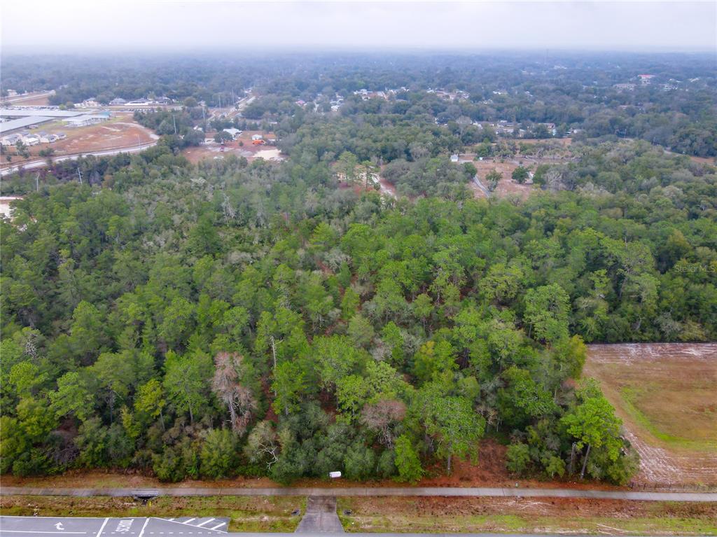 An aerial view shows a wooded lot bordered by a paved road and sidewalk — W RHODE ISLAND AVENUE, ORANGE CITY, FL