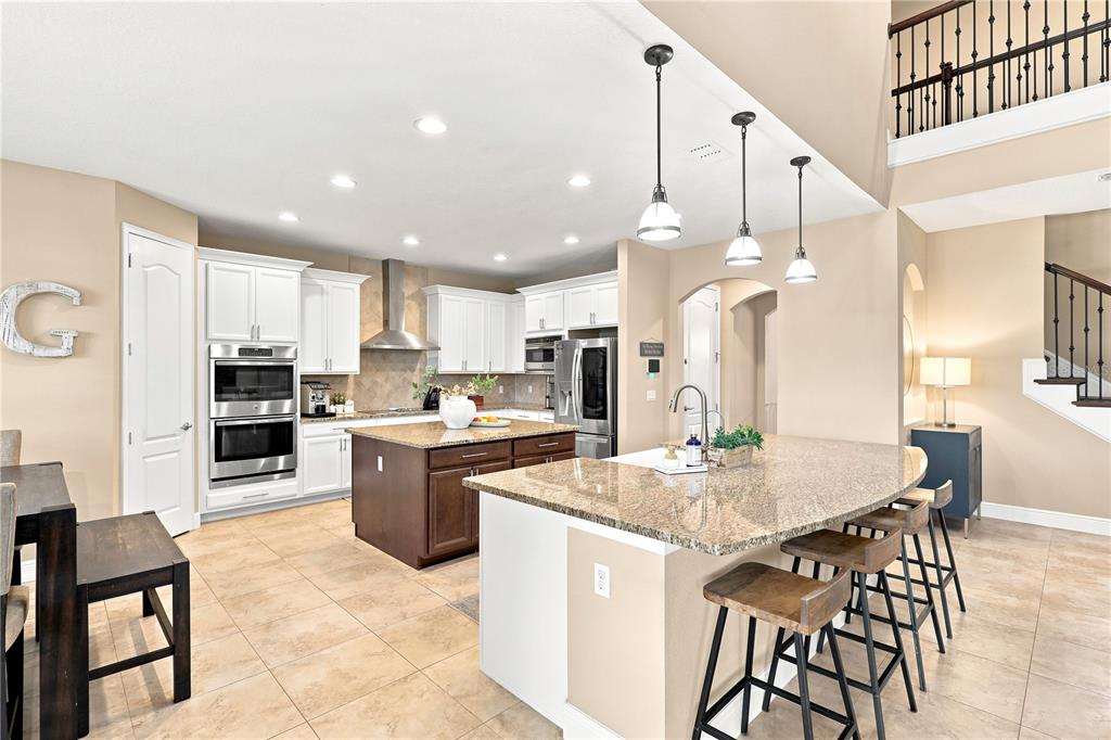 A kitchen features a large granite-topped island, white cabinetry, stainless steel appliances, and tile flooring — 1177 FIELDSTONE CIRCLE, OVIEDO, FL
