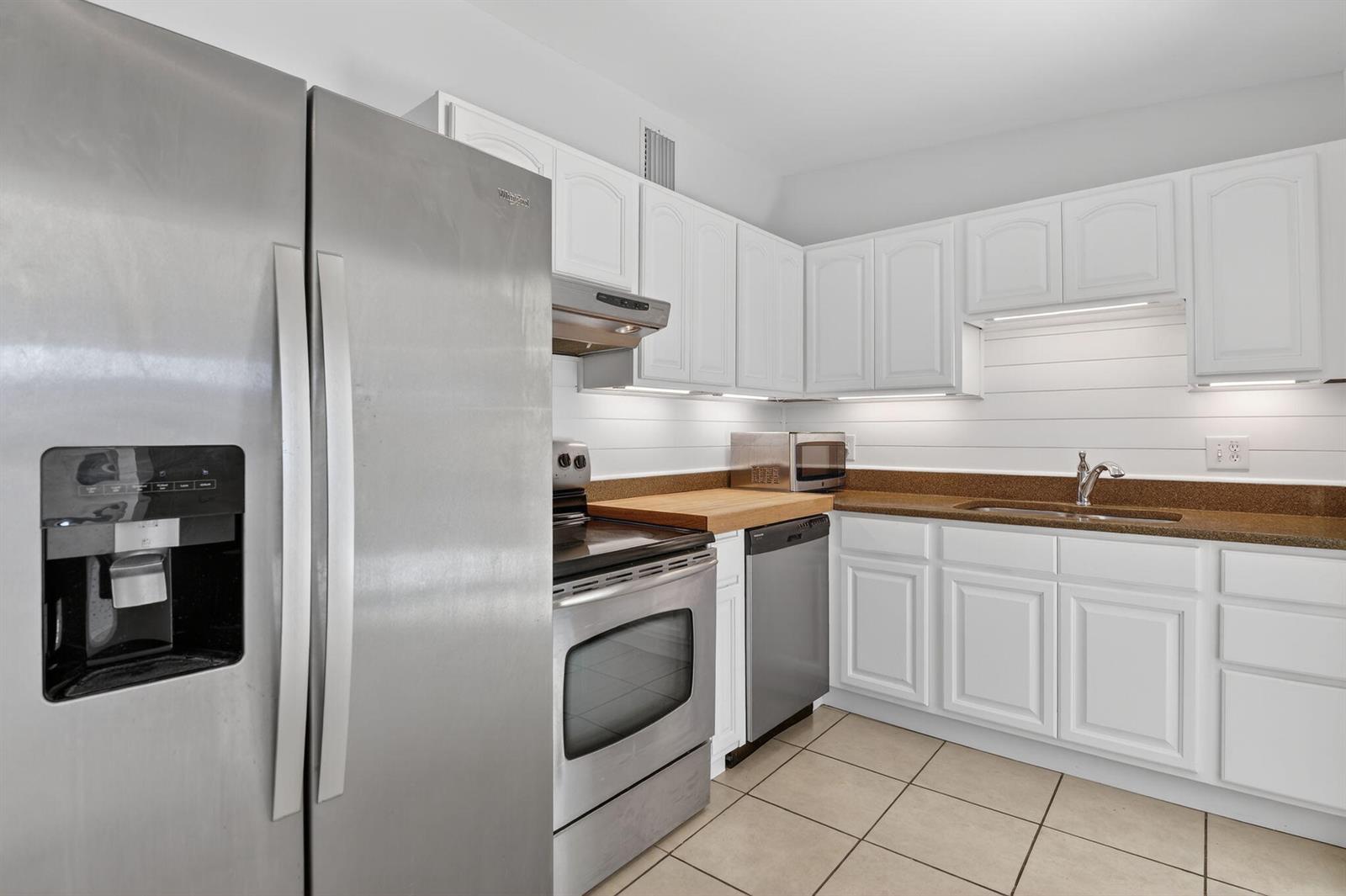 A kitchen features white cabinetry, stainless steel appliances, a brown countertop, and tiled flooring — 1932 Cedarwood Drive, Melbourne FL 32935, MELBOURNE, FL
