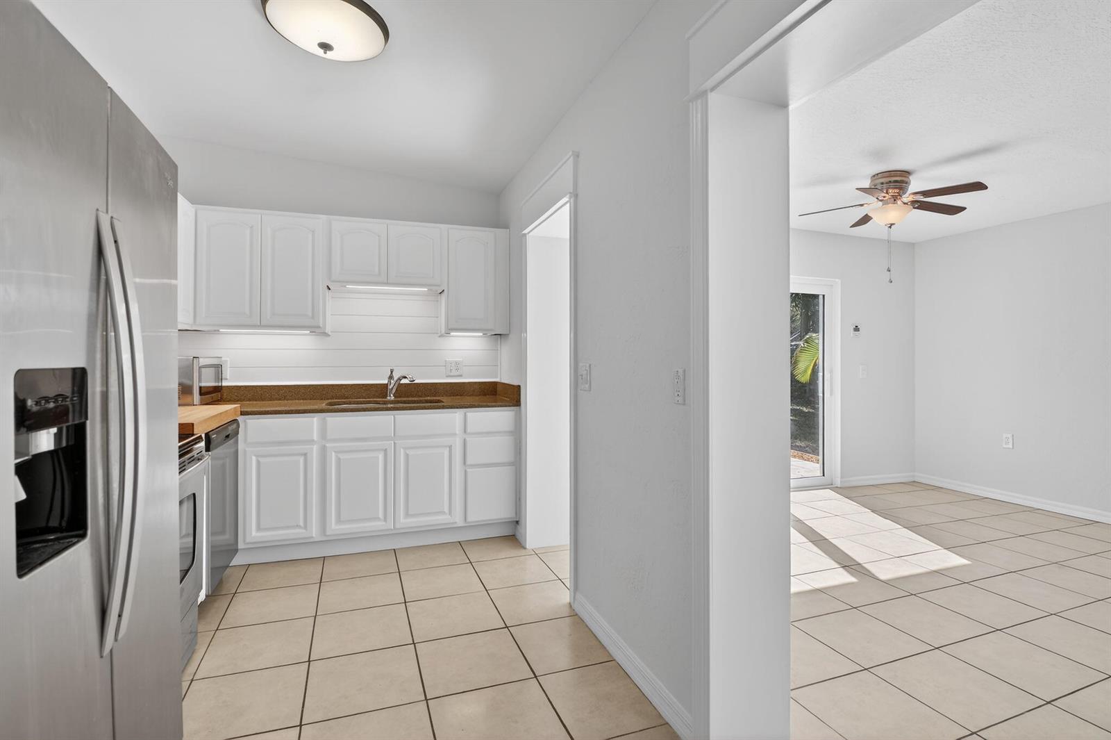 A kitchen with white cabinets and brown countertops opens into a tiled dining area — 1932 Cedarwood Drive, Melbourne FL 32935, MELBOURNE, FL